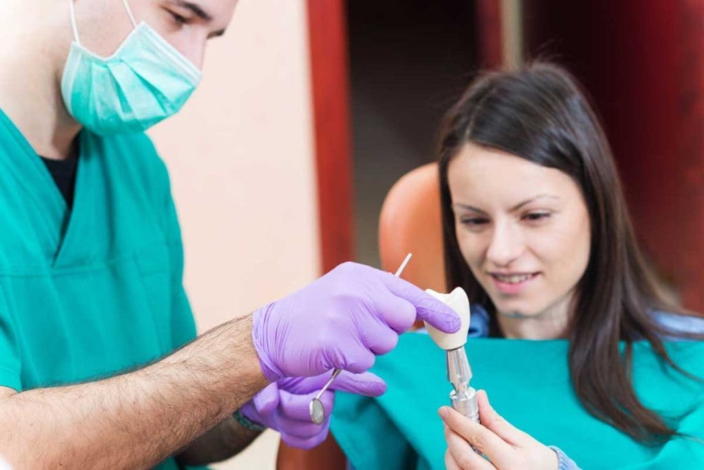 Dentist showing to his patient a dental implant with crown.