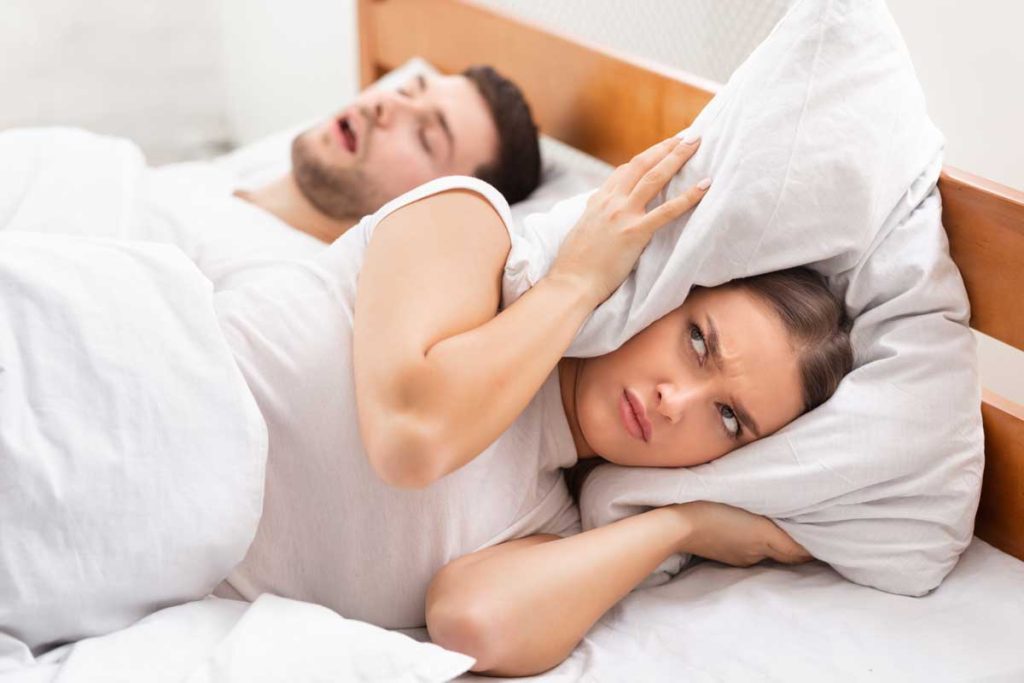 Snoring Concept. Irritated Woman Covering Ears With Pillow Lying Near Sleeping.